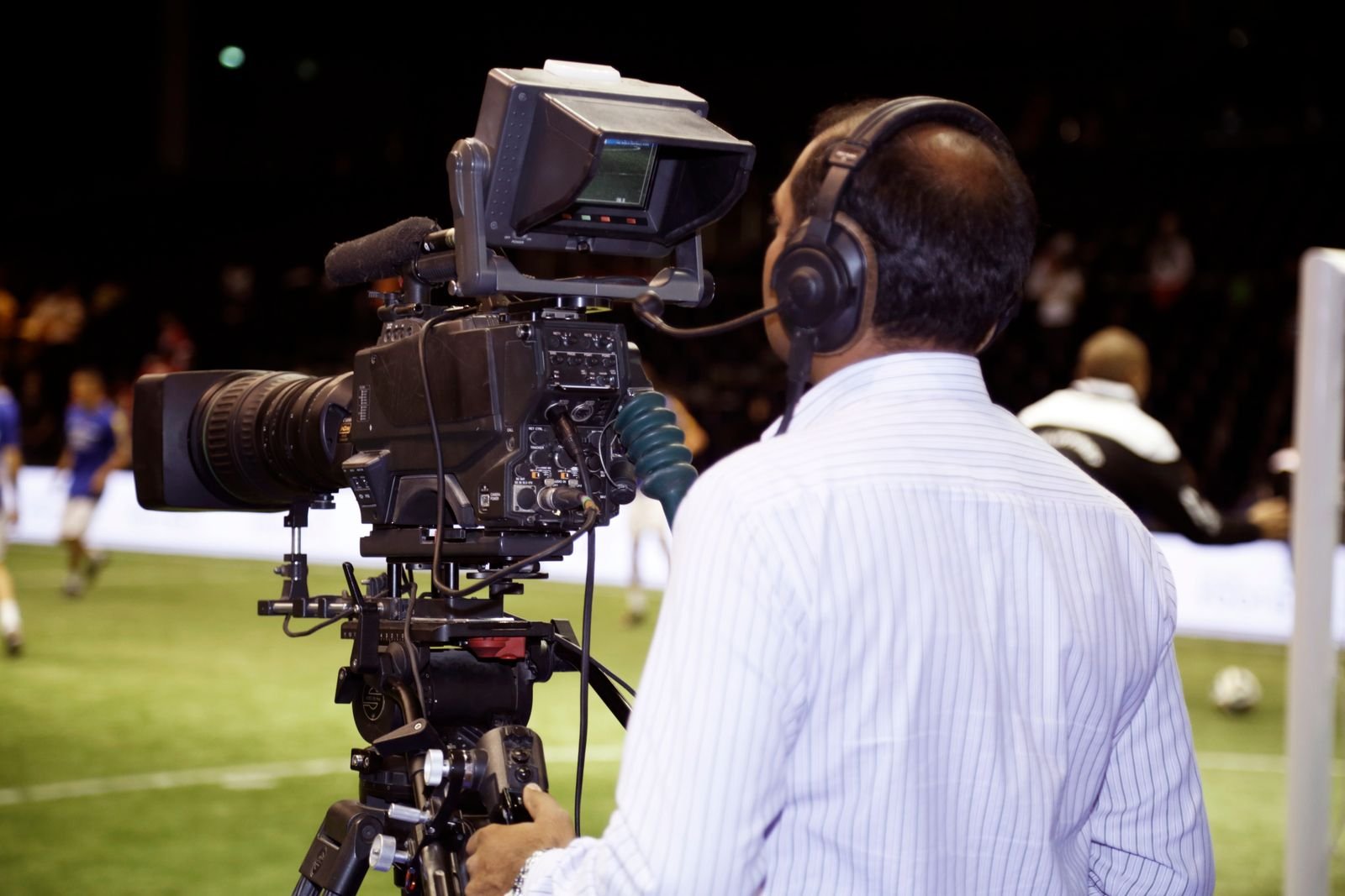 Broadcast camera operator covering a live football match under floodlights